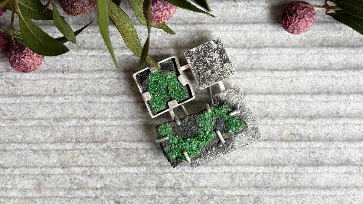 Architectural handmade sterling silver brooch shocasing a brutalist geometric structure contrasted with unpolished green gemstones and organic matrix patterns.