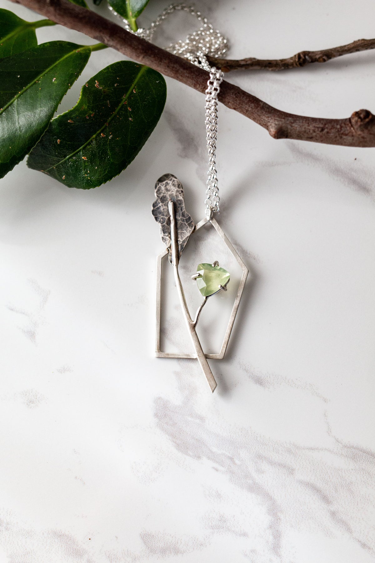 Asymmetric sterling silver pendant with a ttranslucent green prehnite  gemstone and a textured silver leaf, representing the contemporary necklace collection.
