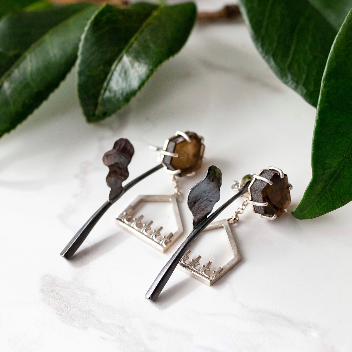 Handcrafted geometric sterling silver earrings featuring raw brown citrine hexagonal slices and oxidised metal leaf and architectural elements, representing the contemporary earrings collection.