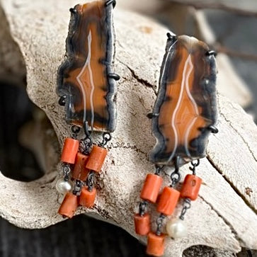 Handcrafted earrings featuring raw edged carnelian agate slices with white crystalline banding, set in oxidised sterling silver claws with a kinetic hanging coral bead and freshwater pearl fringe.